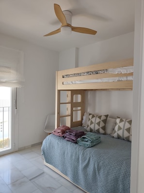 A room with a bunk bed, a ceiling fan, a window with a view, and a door. - New Listing (Rota)