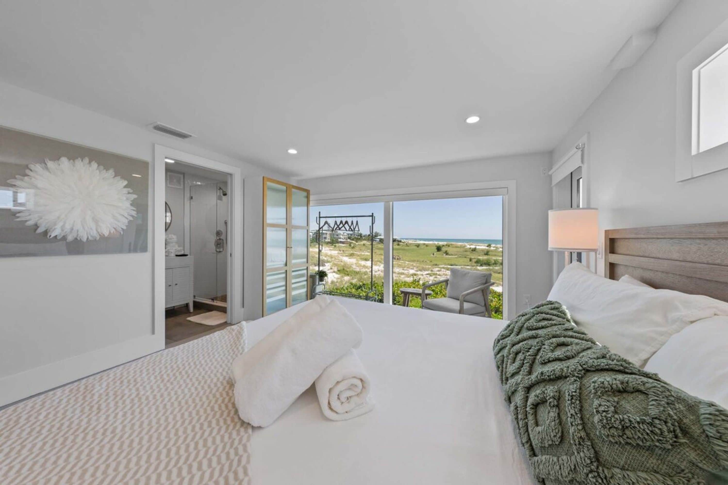 A hotel room with a large bed, a view of the beach, and a balcony with a chair.