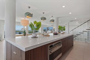 A modern kitchen with a large island, stainless steel appliances, and a view of the outdoors. - Shangri-la - Bean Point - Rooftop Pool -golf Cart (Anna Maria)