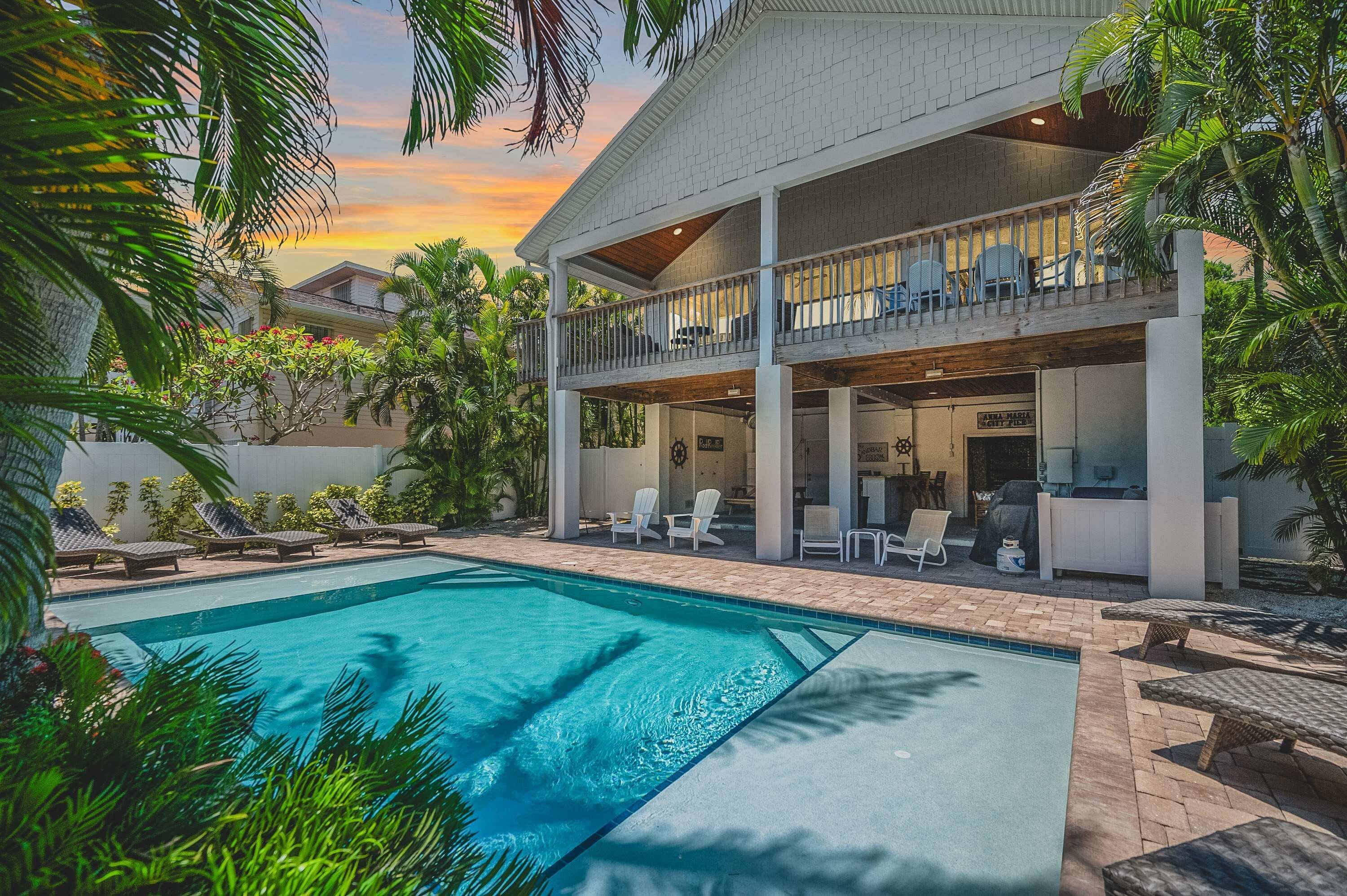 A two-story house with a swimming pool, outdoor seating, and a balcony with chairs.