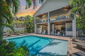 Ein zweistöckiges Haus mit Pool, Außenbereich mit Sitzgelegenheiten und einem Balkon mit Stühlen.