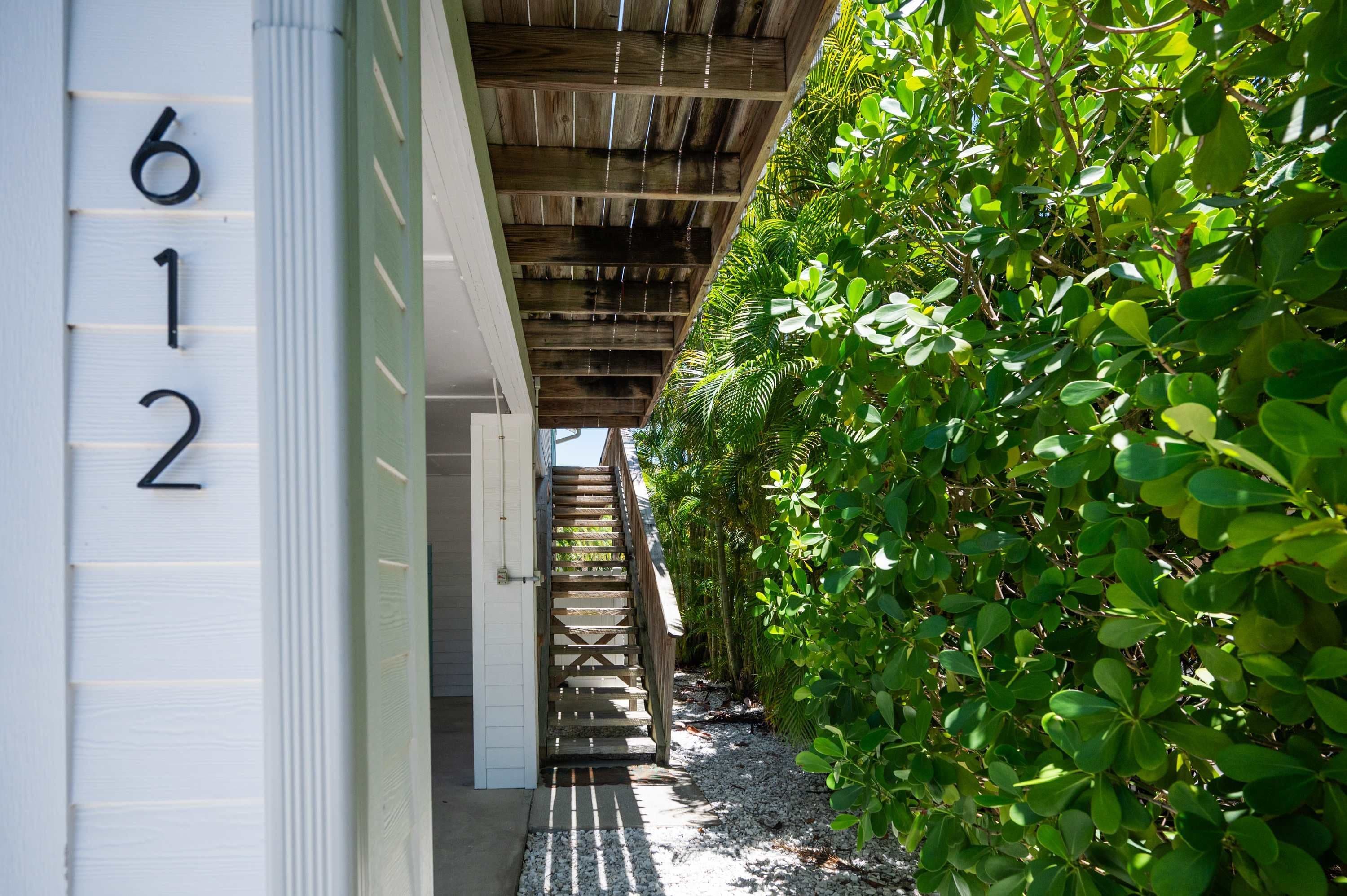 A pathway leading to a building with the numbers 612 on the wall, surrounded by lush greenery.