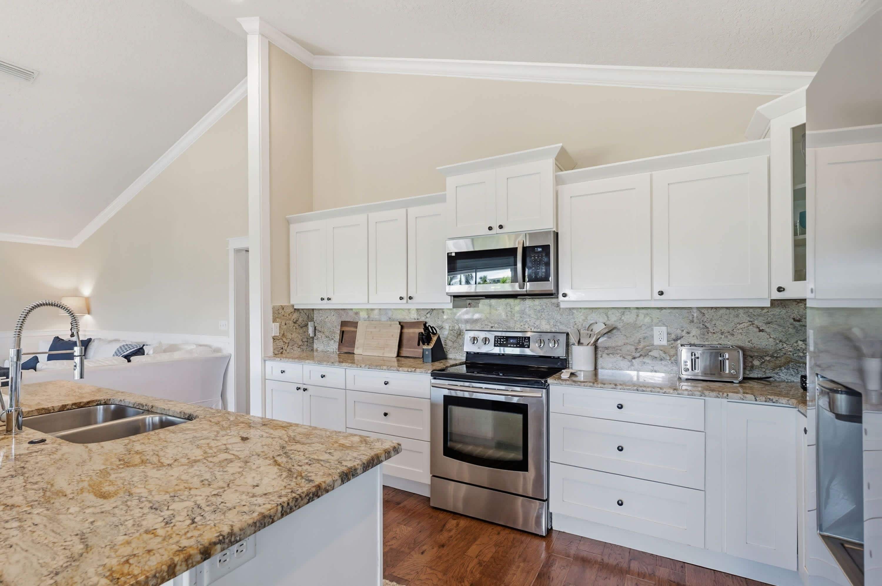A modern kitchen with white cabinetry, stainless steel appliances, and a granite countertop.