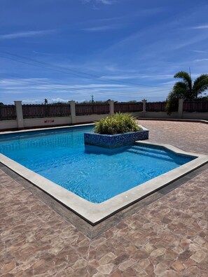 Ein rechteckiger Swimmingpool mit einer gefliesten Kante, umgeben von einer terrassenförmigen Veranda aus Musterstein.