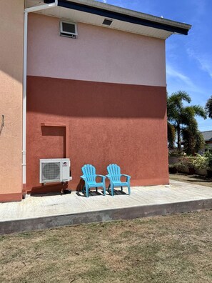 A building with a red and white facade, an air conditioning unit, and two blue chairs outside. - Discover Jam Oasis, Tobago! (Mount Pleasant)