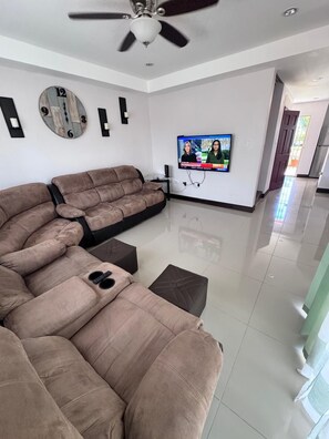 Ein Wohnzimmer mit einem Ecksofa, einem Flachbildfernseher und einem Deckenventilator.