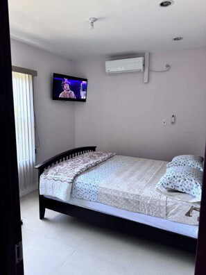 Ein Schlafzimmer mit einem Bett, einem an der Wand befestigten Fernseher und einer Klimaanlage.