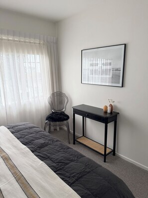 A bedroom with a bed, a chair, a small table, and a framed picture on the wall. - 
The Courtenay - Luxury Urban Retreat (New Plymouth)