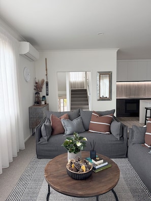 A modern living room with a grey sofa, a coffee table with a plant centerpiece, and a staircase leading to an upper level. - 
The Courtenay - Luxury Urban Retreat (New Plymouth)