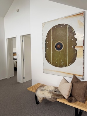 Una habitación con una gran obra de arte circular en la pared, un banco cubierto de piel con almohadones, y una puerta que da a otra habitación.