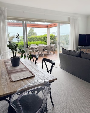 A modern living room with a dining area, a sofa, a TV, and a balcony with a view of greenery. - 
The Courtenay - Luxury Urban Retreat (New Plymouth)