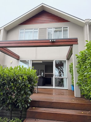 A two-story house with a covered patio, a sliding glass door entrance, and a small garden area with a wooden deck. - 
The Courtenay - Luxury Urban Retreat (New Plymouth)