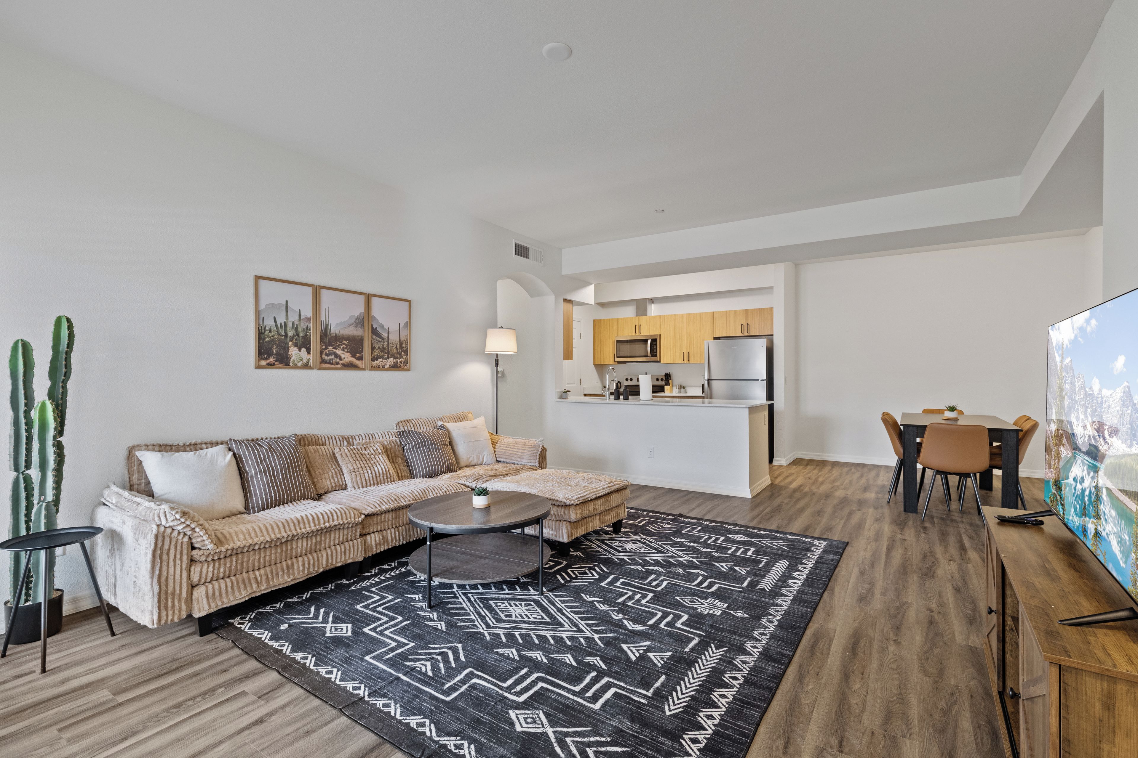 A modern living room with a sofa, coffee table, and a dining area with chairs and a TV.