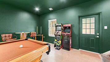 A room with a pool table, two arcade games, a door, and a window.