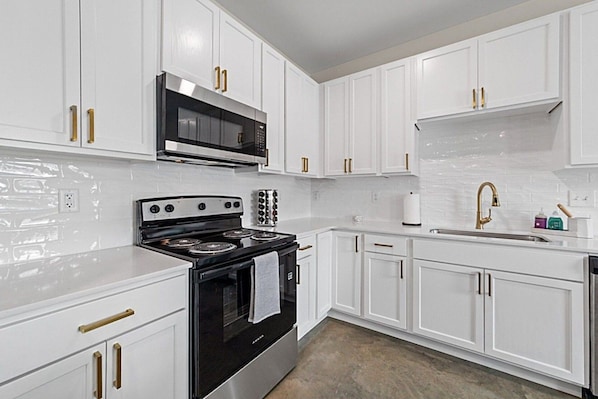 A kitchen with white cabinets, a black stove, a microwave, and a gold faucet.