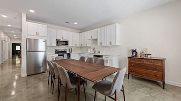 A modern kitchen with white cabinets, stainless steel appliances, and a wooden dining table with chairs.