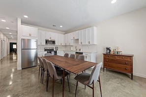 A modern kitchen with white cabinets, stainless steel appliances, and a wooden dining table with chairs.