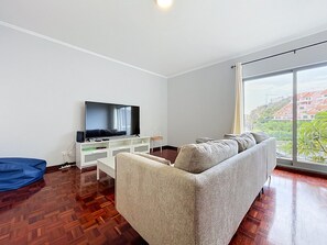 Un soggiorno moderno con una TV a schermo piatto, un divano e un'ampia finestra vista edifici.