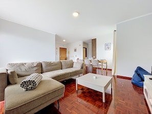 A living room with a sofa, a coffee table, and a dining area with chairs and a table. - Palmeira Apartment by Atlantic Holiday (Santa Cruz)
