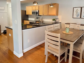 A kitchen with wooden cabinets, a stainless steel microwave, and a wooden dining table with chairs. - Beautiful 4 bedroom home on the bike trail and east of Rt 1! (Lewes)