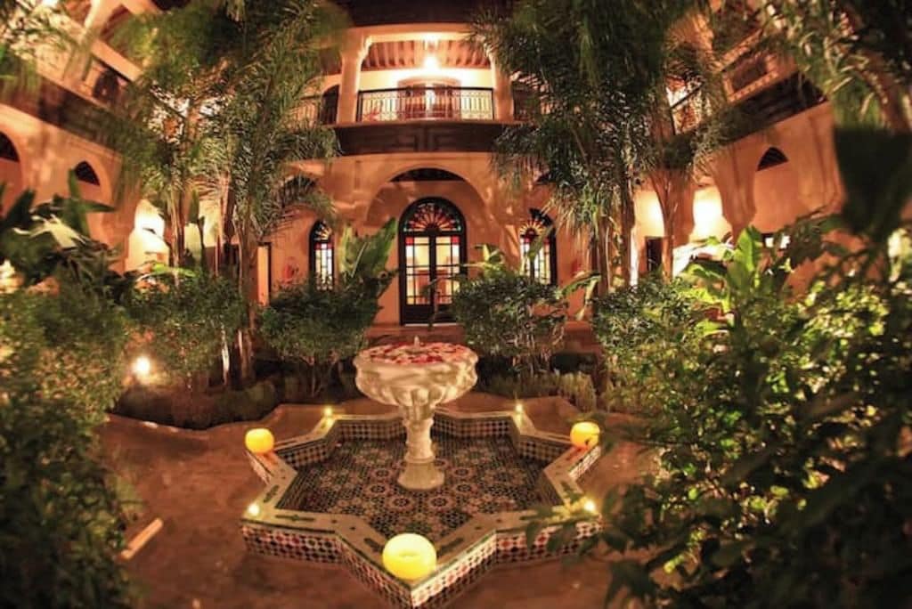 Un patio con una fuente, rodeado de abundante vegetación y arquitectura tradicional.