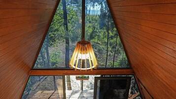 A triangular wooden room with a hanging light fixture and a view of the forest.