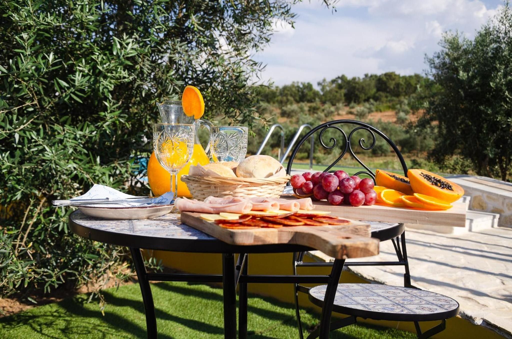 Une table à manger installée à l’extérieur, sur laquelle on trouve une variété de plats et de boissons, le tout mis en valeur par un décor de verdure et un chemin pavé de pierres.
