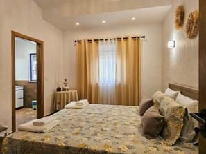 Ein Hotelzimmer mit Bett, Nachttisch, Spiegel, einem Fenster mit Vorhängen und einer Wandleuchte.