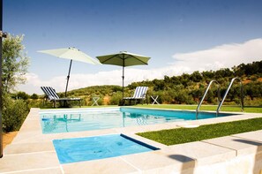 Una piscina amb dues gandules i ombrel·les, envoltada d'un jardí ben condicionat.