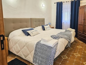 A double bed with a beige headboard, two pillows with text, a bedside lamp, and a blue curtain.