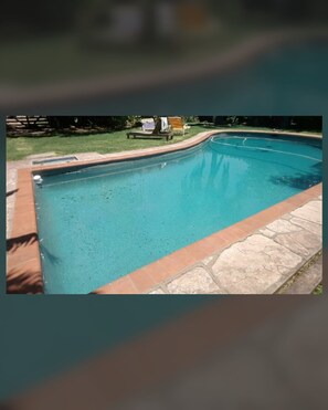 A swimming pool with a stone border and a grassy area with a bench and a chair. - New Listing (Monte Grande)