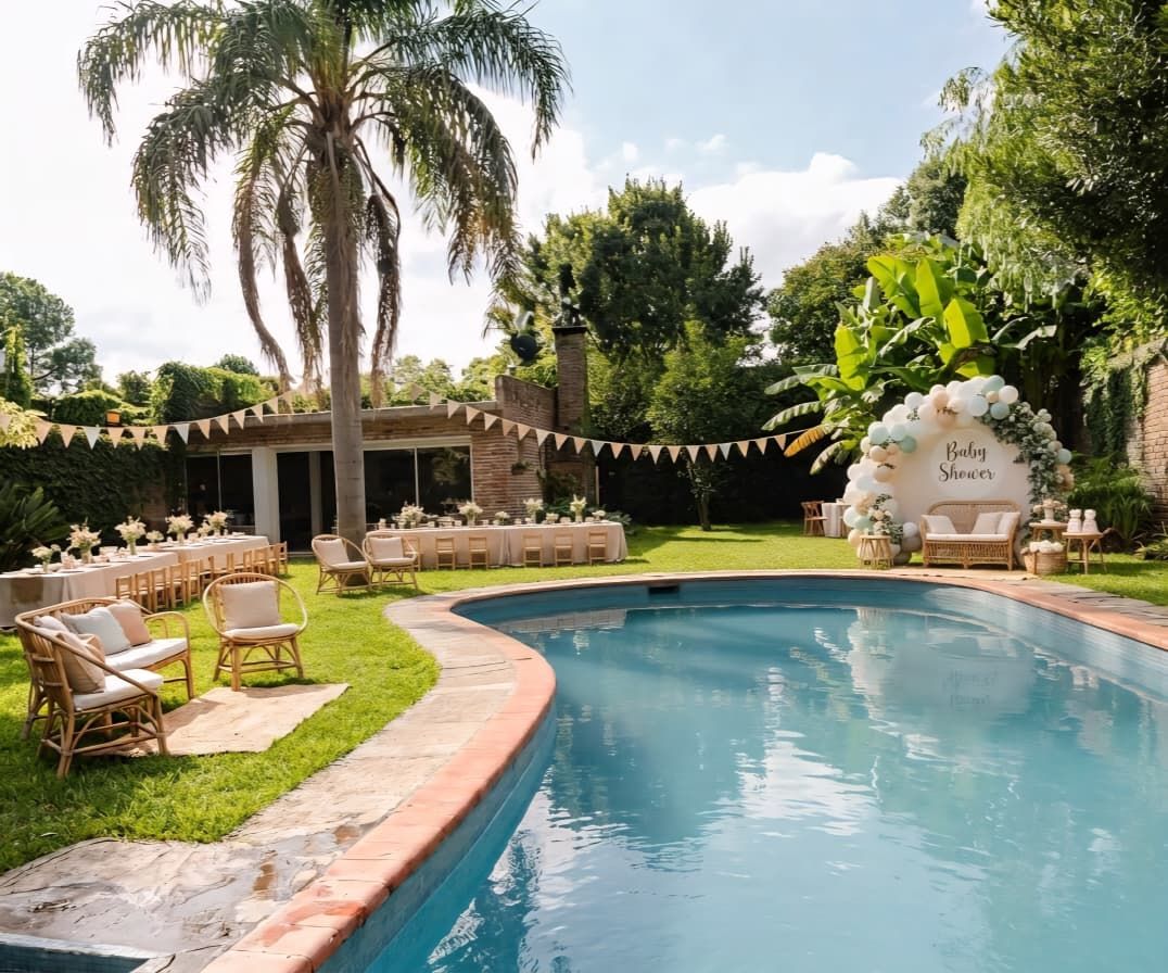 An outdoor pool area with lounge chairs and tables, surrounded by greenery and a covered seating area.