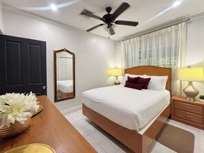 Une chambre d’hôtel avec un lit, des lampes de chevet, un ventilateur de plafond, un miroir, une porte et une table agrémentée d’un arrangement floral.