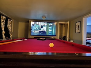 A pool table with a single yellow ball, a television displaying a room, and a door leading to another space. - TheGoodTimes House! Hot Tub+GameRoom+petsok! (Lake Harmony)