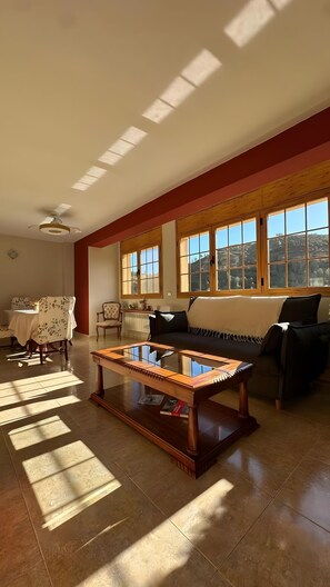 A spacious living room with a large window, a ceiling fan, a wooden coffee table, and a sofa. - Apartment 'Ca La Cabrera' with Mountain Views, Private Terrace and Wi-Fi (Alfara de Carles)