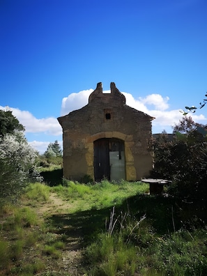 A small stone building with a single door and a small window, surrounded by greenery and a clear sky. - Apartment 'Ca La Cabrera' with Mountain Views, Private Terrace and Wi-Fi (Alfara de Carles)