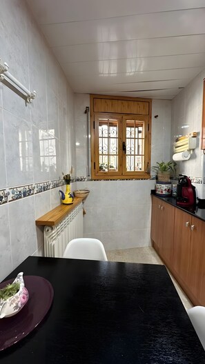 Une cuisine de taille réduite, dotée d’un meuble en bois, d’un plan de travail noir et d’une fenêtre ornée de barreaux en fer décoratifs.