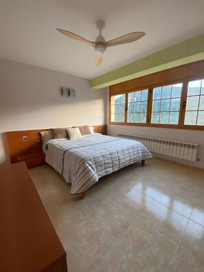 A bedroom with a bed, a ceiling fan, a window with a view, and a radiator. - Apartment 'Ca La Cabrera' with Mountain Views, Private Terrace and Wi-Fi (Alfara de Carles)
