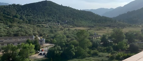 Vista da un balcone su una valle con montagne all'orizzonte, un edificio con un silo e cielo sereno.