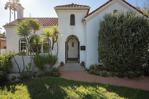 A white building with a tiled roof, a central arched entrance, and a small window above the door. - Hauser House l Artful Spanish-Style Bungalow (Los Angeles)
