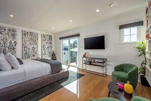 A modern bedroom with a large bed, a flat-screen TV, and a sliding glass door leading to a balcony. - Hauser House l Artful Spanish-Style Bungalow (Los Angeles)