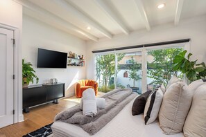 A modern bedroom with a bed, a TV, a sofa, and a sliding glass door leading to a balcony. - Hauser House l Artful Spanish-Style Bungalow (Los Angeles)