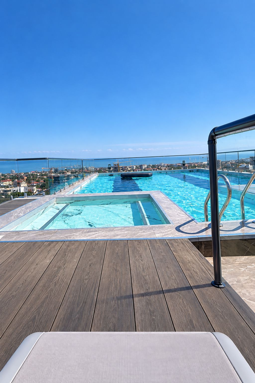 A pool with a view of the city and sea, surrounded by a wooden deck.