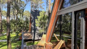 A deck with wooden flooring, two wooden chairs, and a glass door leading to a covered area.