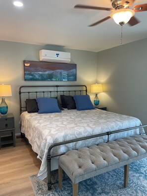 A bedroom with a bed, bedside tables, a ceiling fan, an air conditioning unit, and a painting on the wall. - Key Colony Beach House with Cabana Club Access (Key Colony Beach)