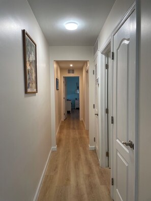 A hallway with a wooden floor, white walls, and a ceiling light. There are doors on the right and a framed picture on the left. - Key Colony Beach House with Cabana Club Access (Key Colony Beach)