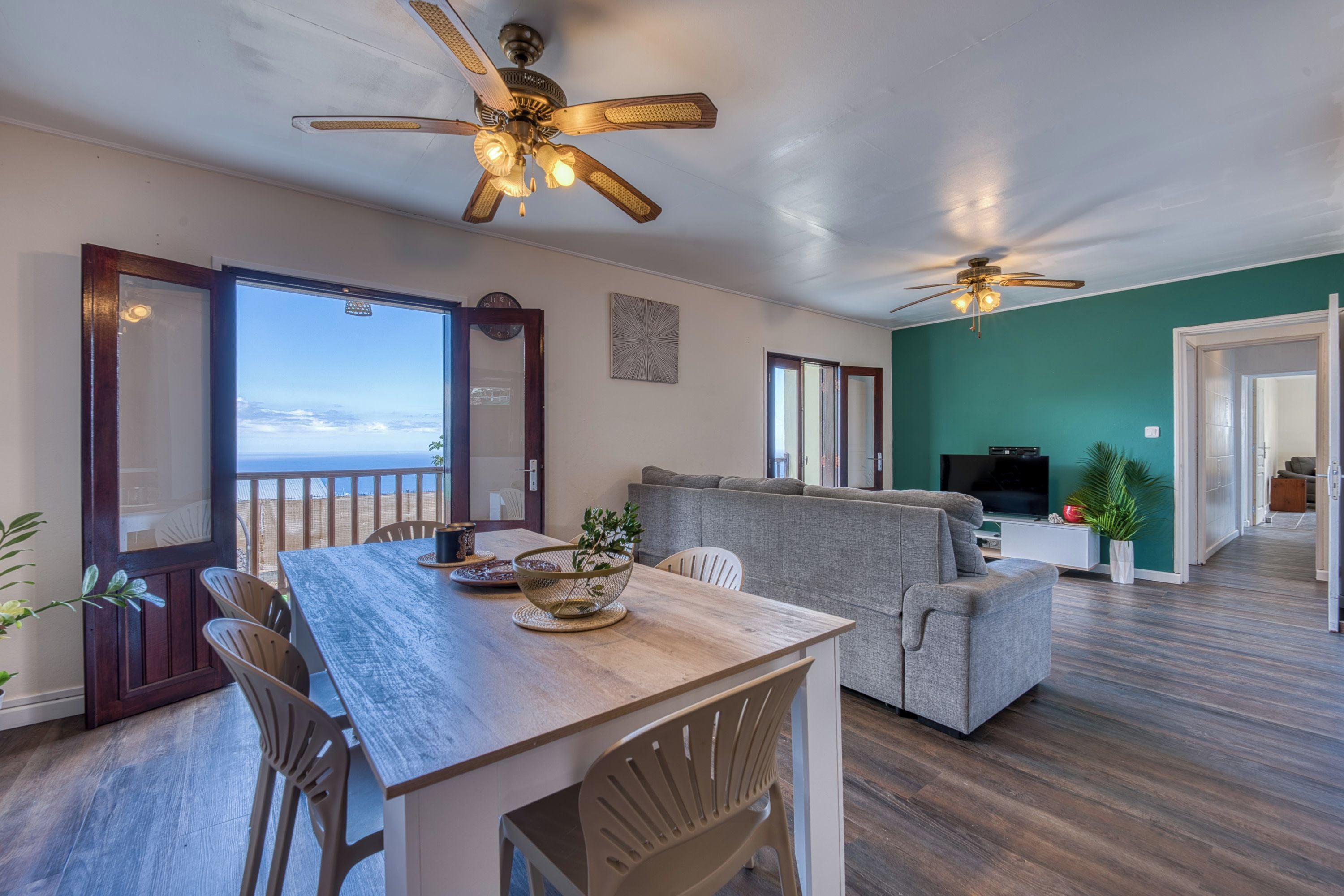 A spacious living area with a wooden dining table, a grey sofa, and a ceiling fan.