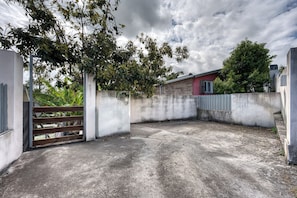 A concrete courtyard with a metal gate, surrounded by walls and vegetation. - Ker Papangue - Terrasse - Wifi (Saint-Louis)