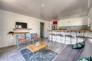 A compact living space with a sofa, two chairs, a coffee table, a TV, a kitchen area with a microwave, and a small bar counter with stools. - Ker Papangue - Terrasse - Wifi (Saint-Louis)