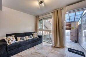 A modern living room with a dark sofa, patterned cushions, and a glass door leading to a balcony. - Ti'Bulle - Petfriendly - Jacuzzi (Saint-Pierre)